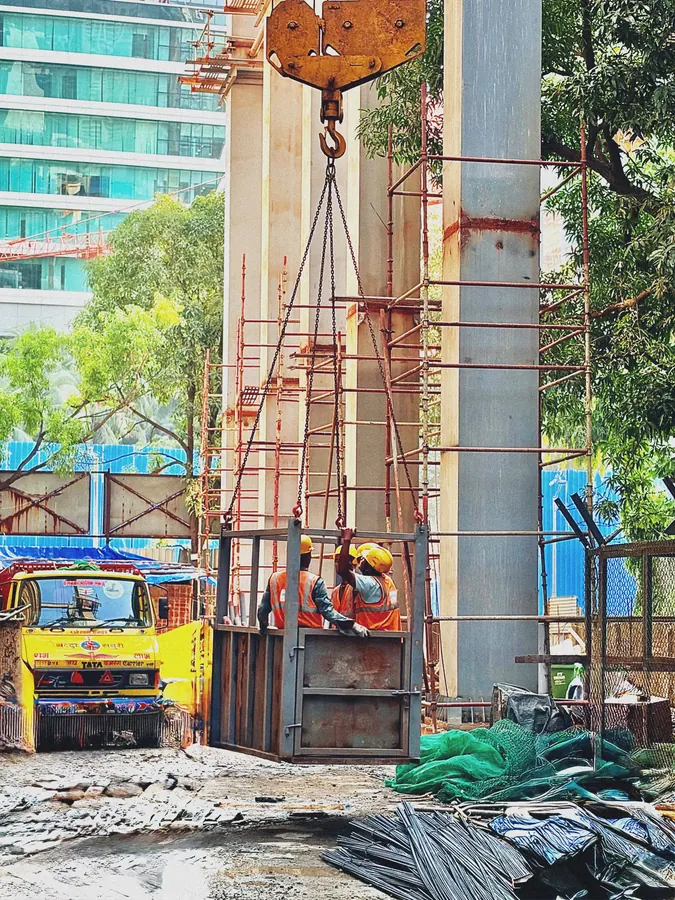 Construction workers guiding a crane lift beside scaffolding and concrete columns