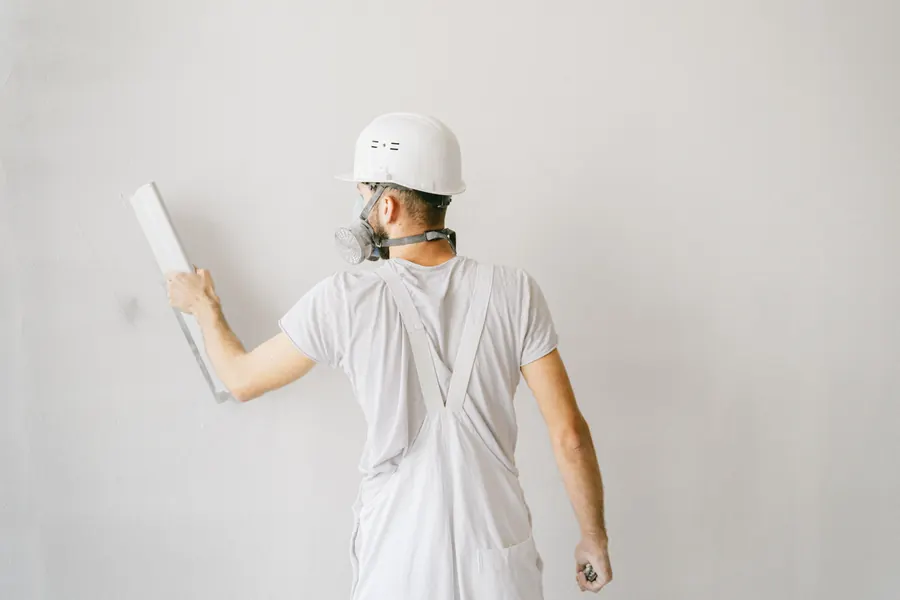 Construction worker smoothing a light interior wall with a long finishing tool